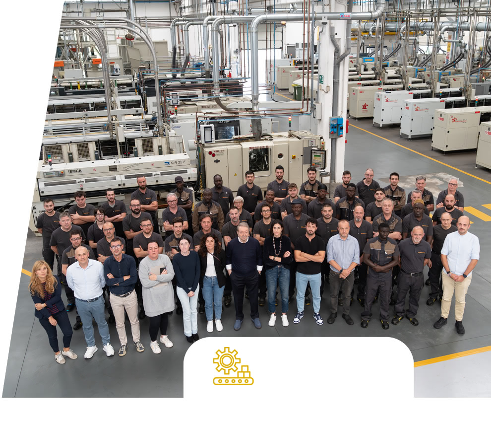 Photo de groupe de l'équipe Eredi Baitelli en atelier, avec les lignes de production et les machines en arrière-plan.